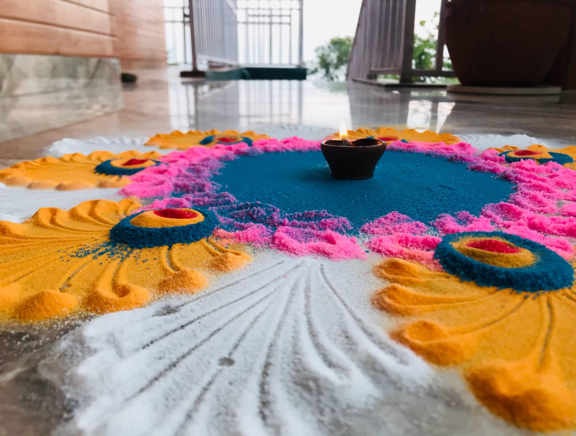 A white, red, blue and pink rangoli with a small lamp in the muddle of the design.