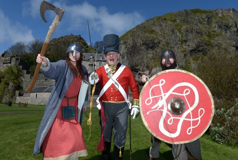 Three reenactors in different period costumes in front of a castle.