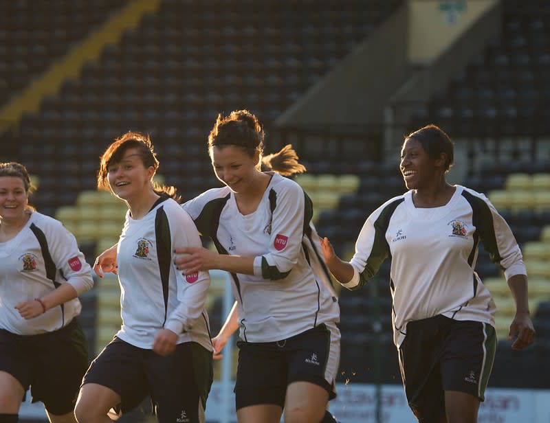 Women playing football in a University team - close up on four women - three are white and one is Black. They are laughing as they are running in football strip.