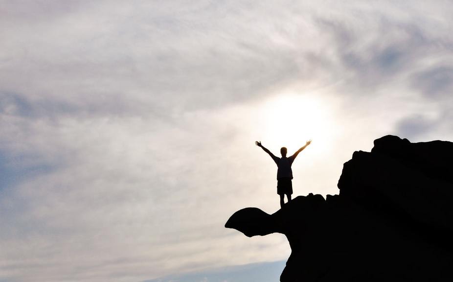 A person standing at the top of a cliff with arms raised