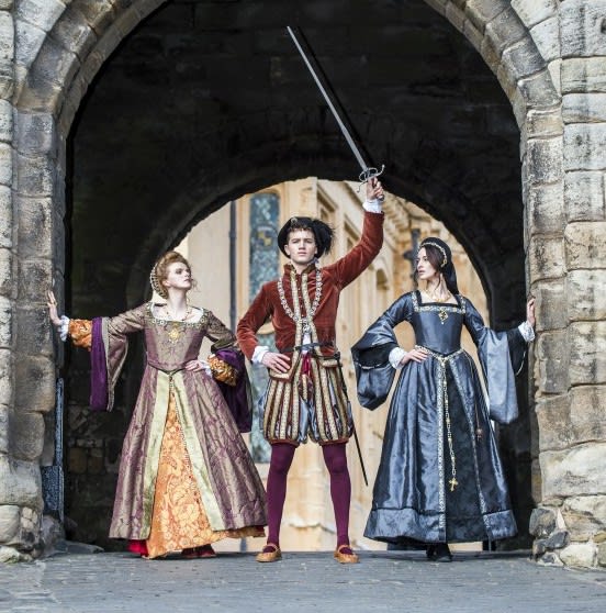 Two ladies standing on each side of a young man waving a sword, all in Renaissance costume.