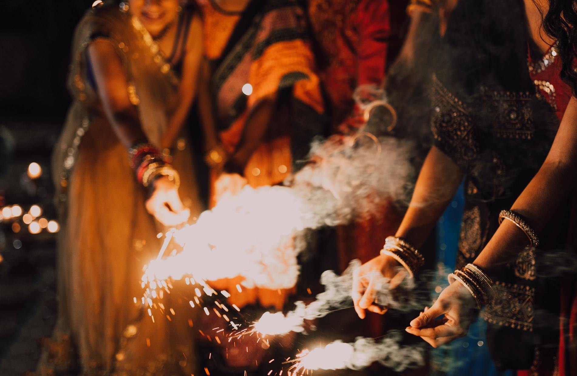 A group of South Indians in colourful clothing play with sparklers at night