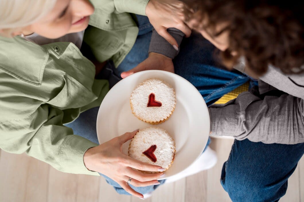 Two people sharing a plate with two identical cakes with with icing sugar on top and hearts in the middle.
