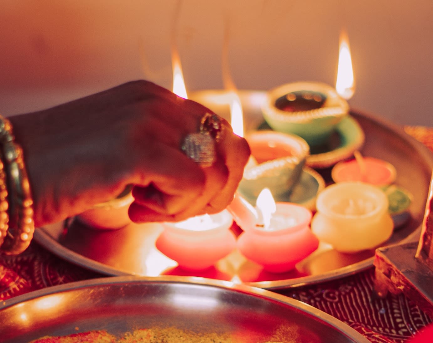 A woman's hand lights some cute pastel oil lamps on a metal tray.