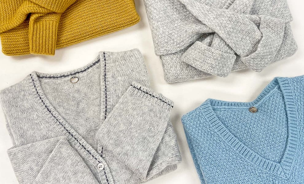 Flatlay image of four neatly folded blue, grey and yellow sweaters.