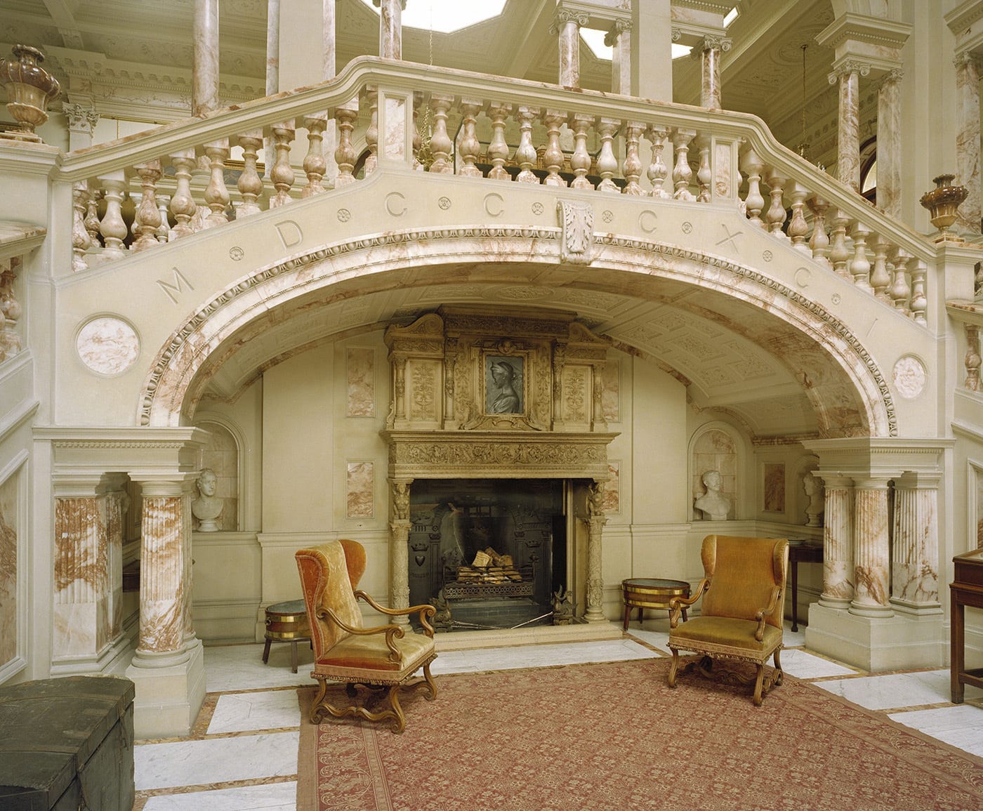 A marble staircase and large marble hallway, with two armchairs in front of a fireplace