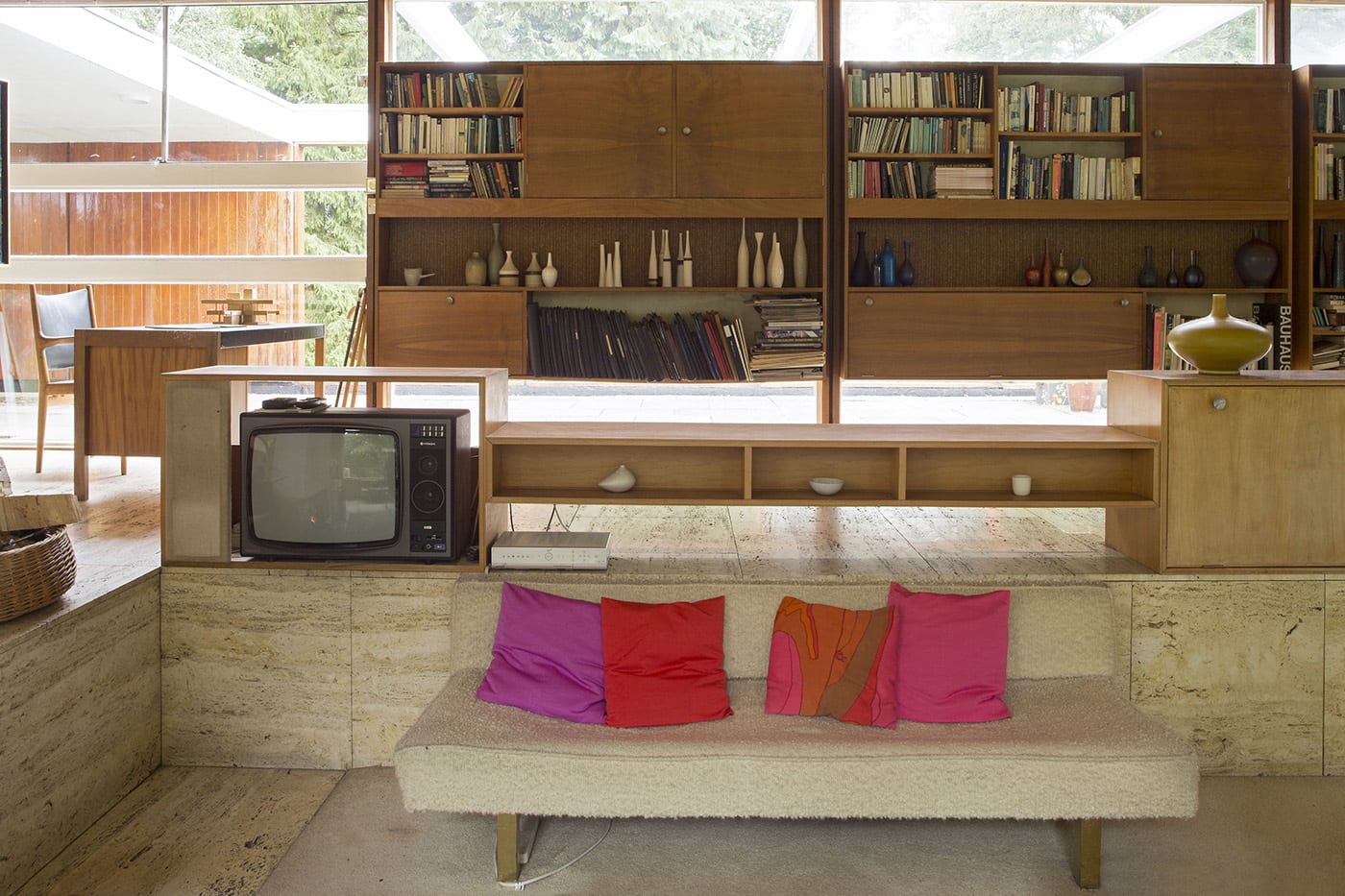 A living room with a small sofa, old TV, and shelving units filled with books and ornaments