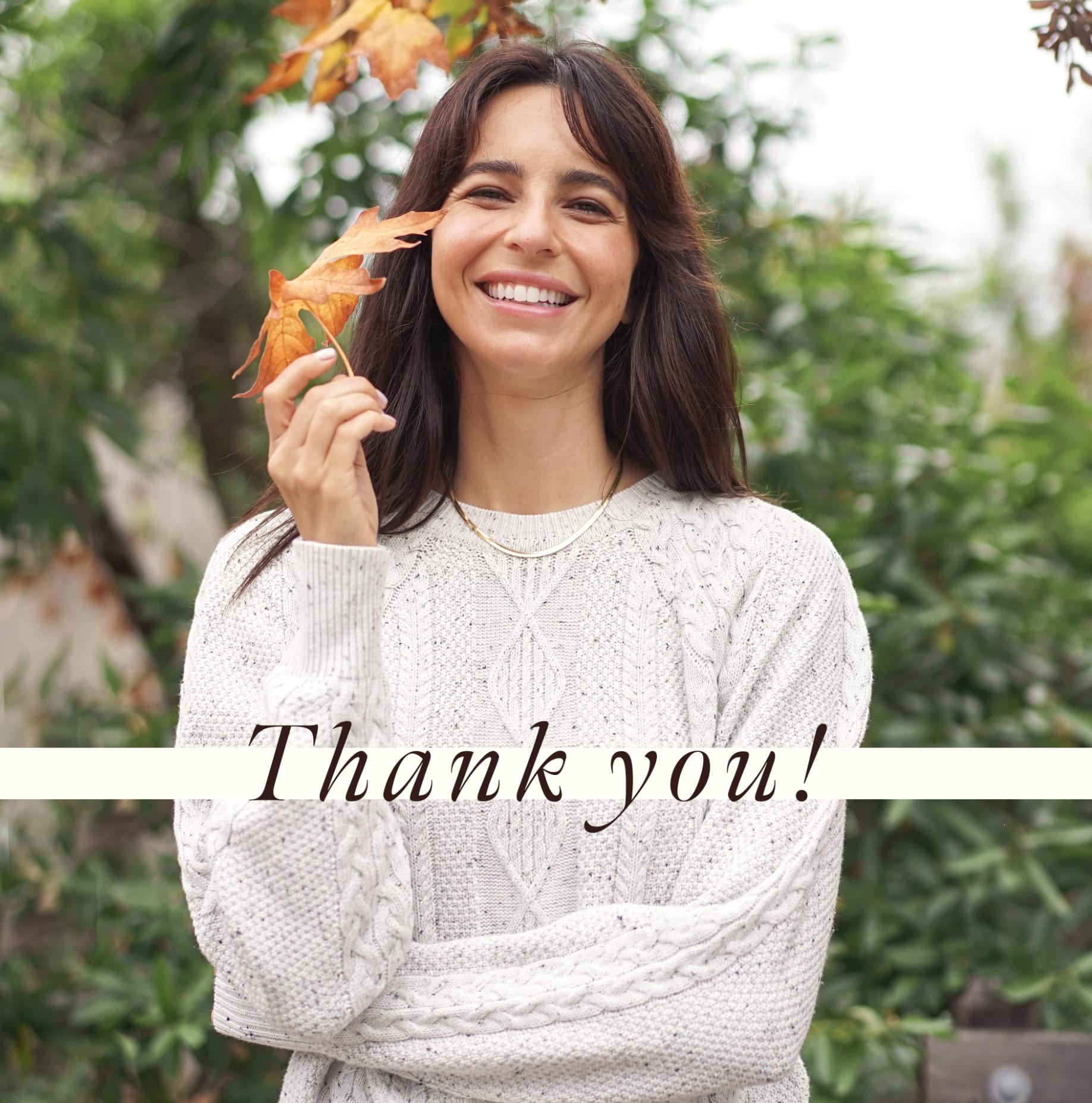 Smiling woman holding a fall leaf and wearing a white cord sweater. Overlaying italic text says "Thank you!".