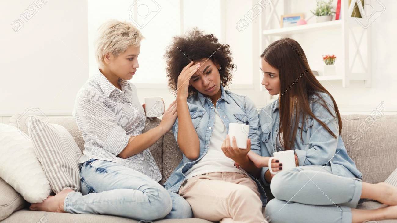 97692404-young-women-talking-and-consoling-their-sad-friend-casual-girls-sharing-problems-at-home-unity-and
