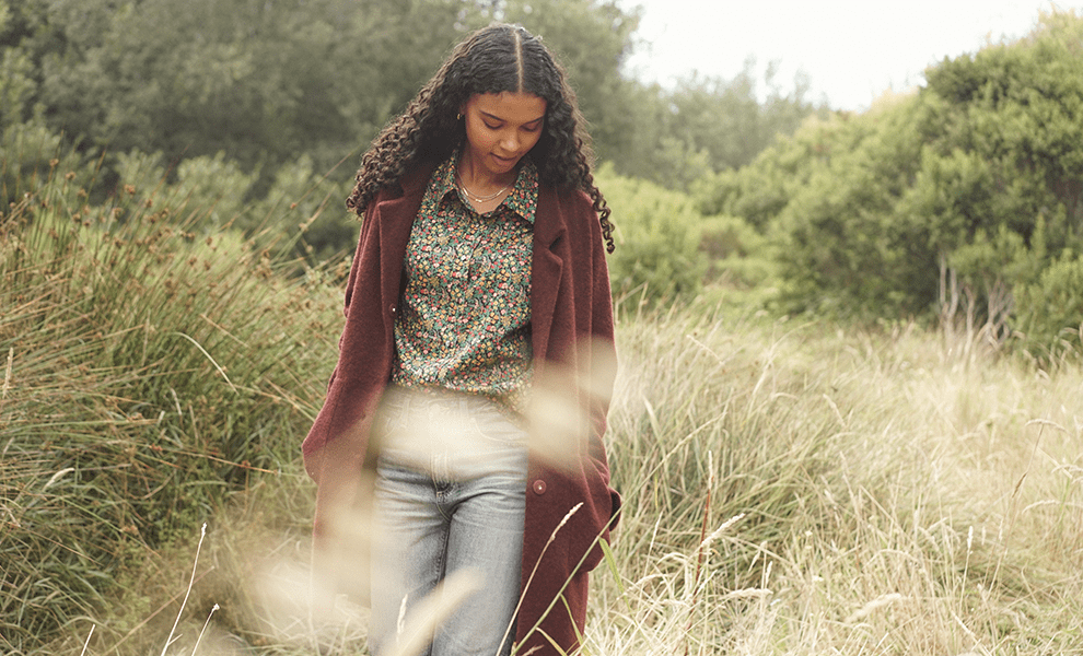 Woman walking through a grass filed wearing a burgundy coat.