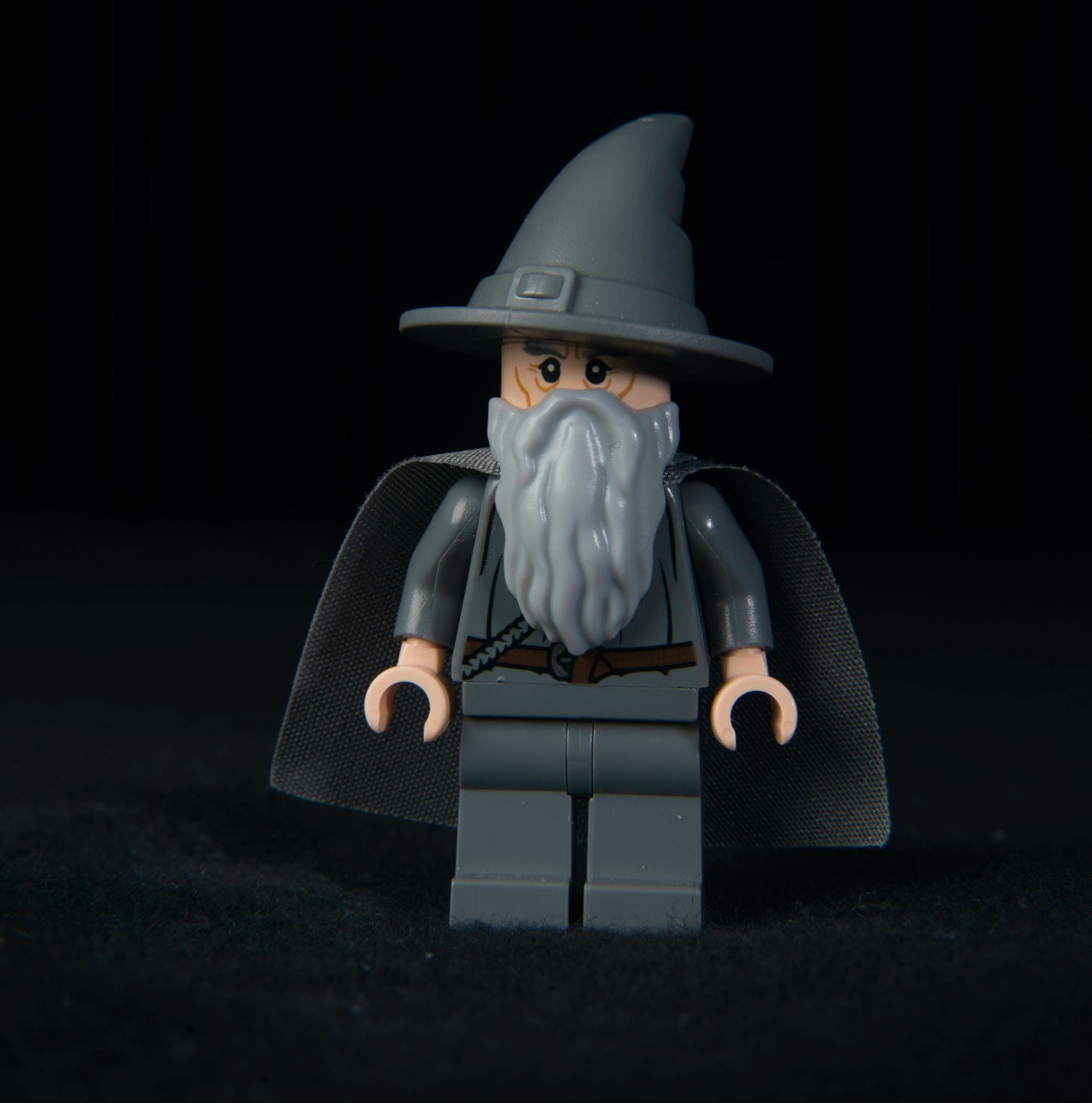 A lego character of Gandalf the Wizard - they have a long grey beard, a grey cloak a sombre expression and a big pointy grey hat.