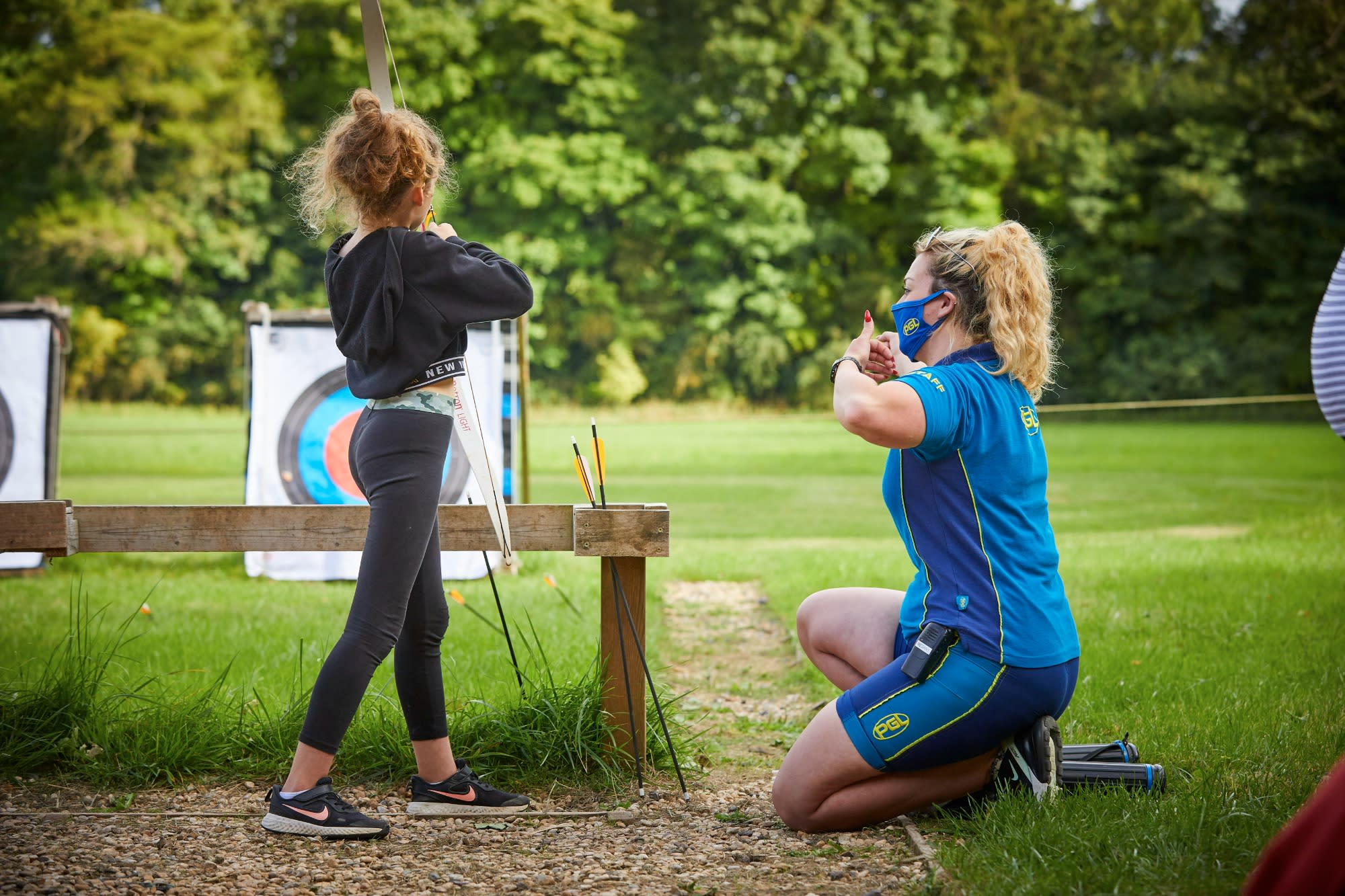 A PGL instructor gives a girl doing archery a thumbs up as she aims at the target