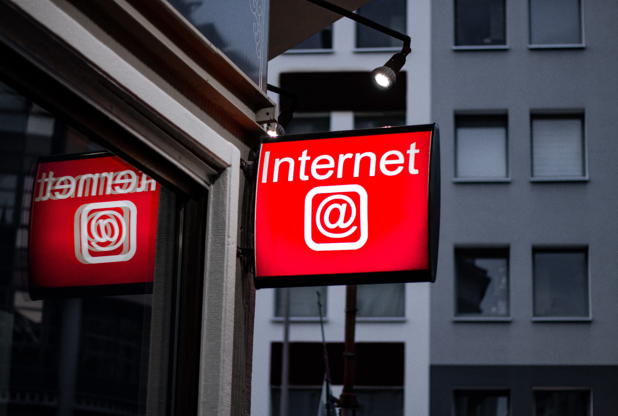 A red and white lit sign with 'internet' on it and the @ sign - with grey and white buildings in the background