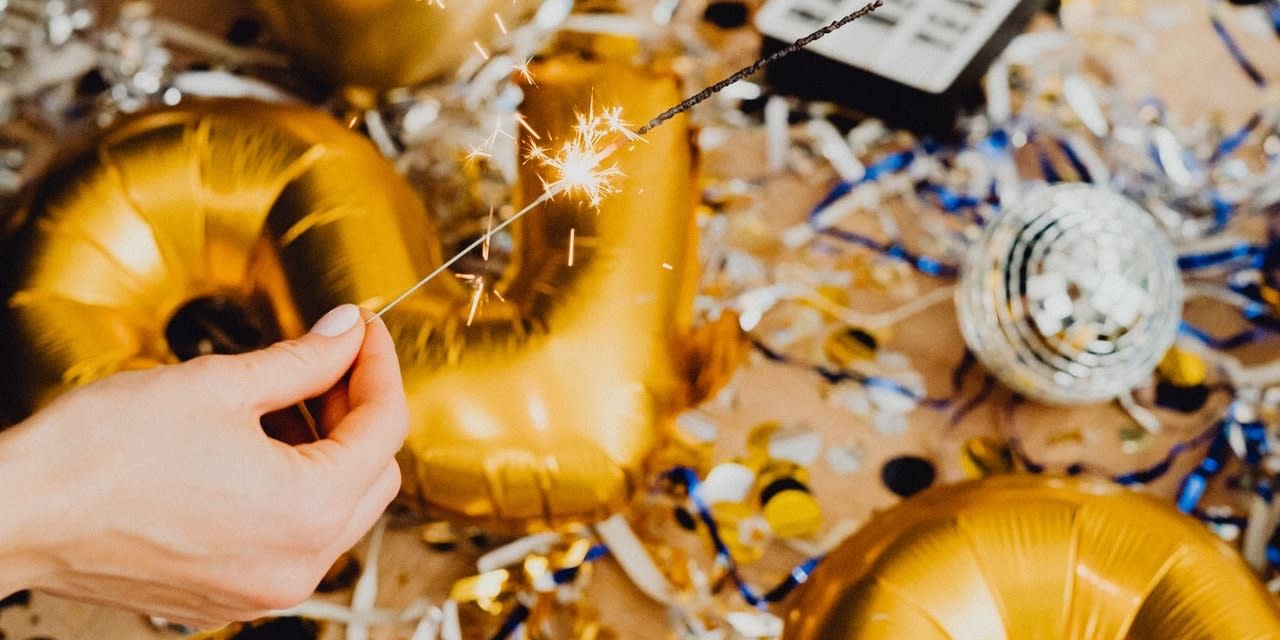 A woman's hand holding a sparkler over a background of vinyl balloons and confetti