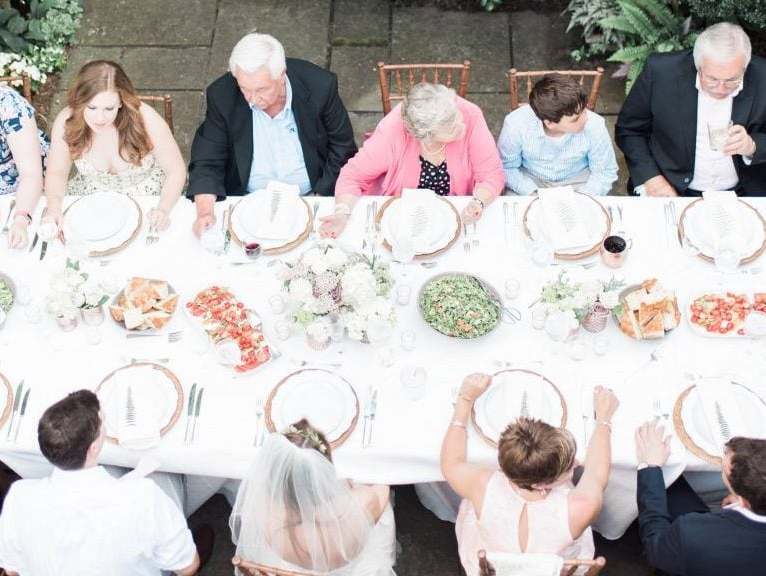 Arial shot of an intimate wedding party sharing dinner at a long rectangular table set with white linens