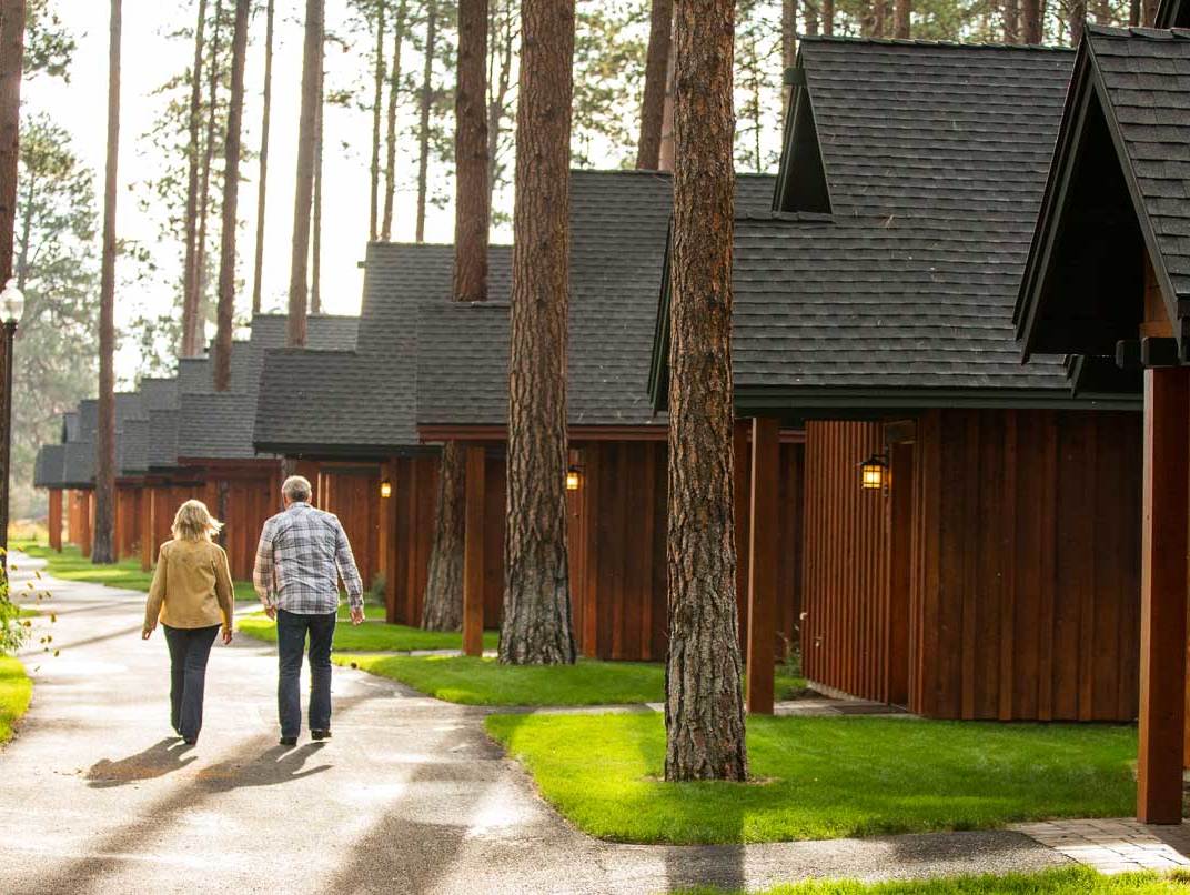 a man and woman walk along a row of identical brown cabins