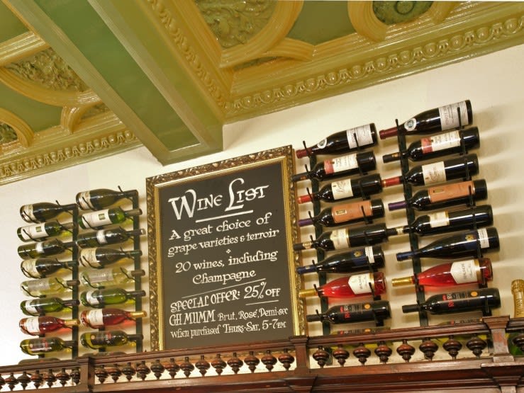 Bottles of wine stacked up on racks around a chalkboard advertising the wine list.