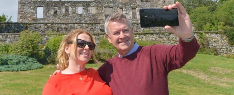 Man and woman posing to take a selfie in front of a castle.