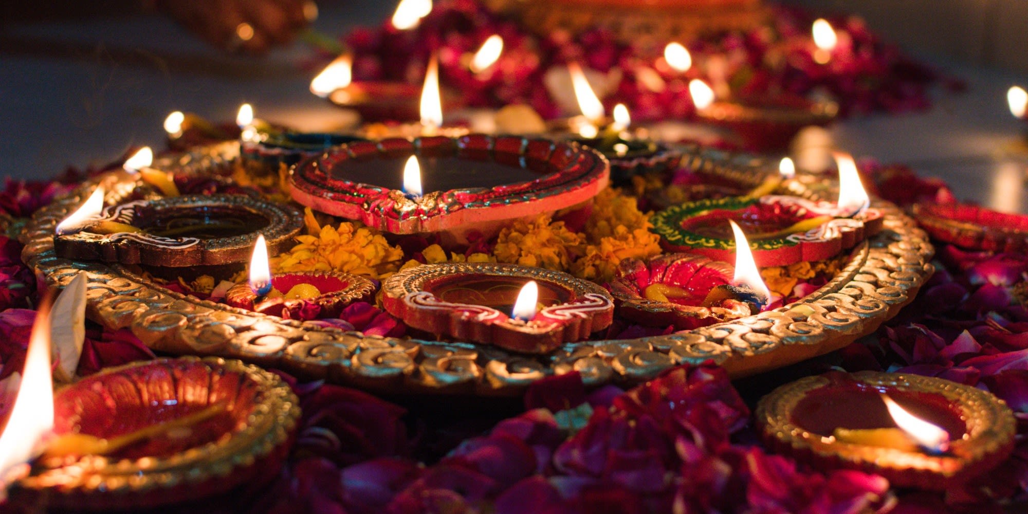 A tray of lit oil lamps, resting on flower petals