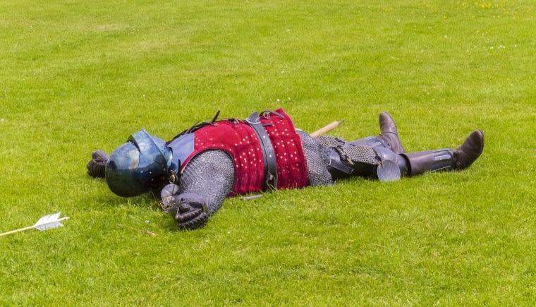 Warrior in chainmail and helmet lying flat on his back on the grass.
