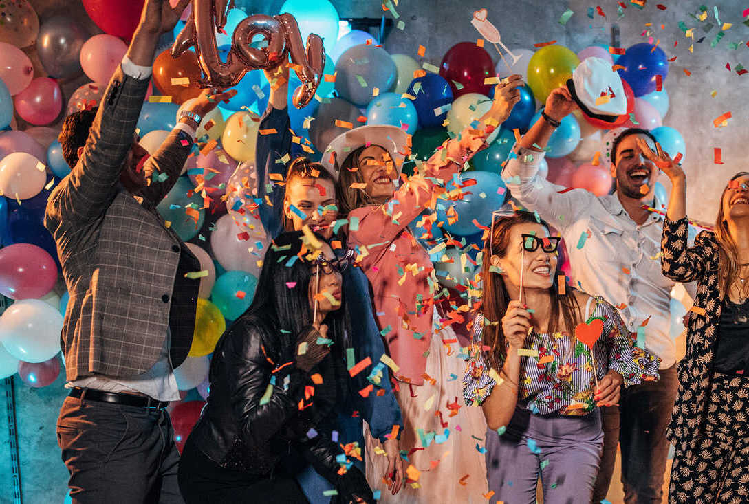 people celebrating at a party decorated with bright colored balloons and confetti