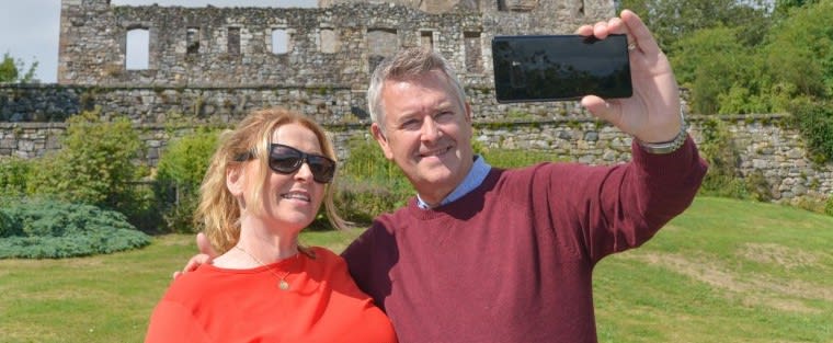 Man and woman posing to take a selfie in front of a castle.